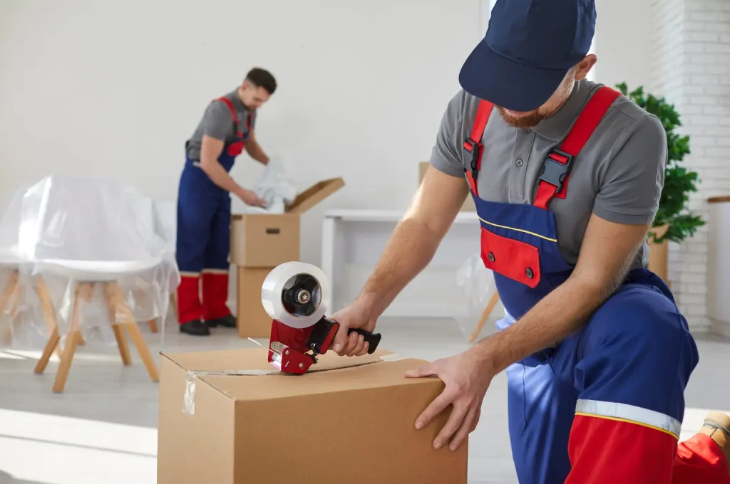 Two professional movers packing and taping cardboard boxes in a home